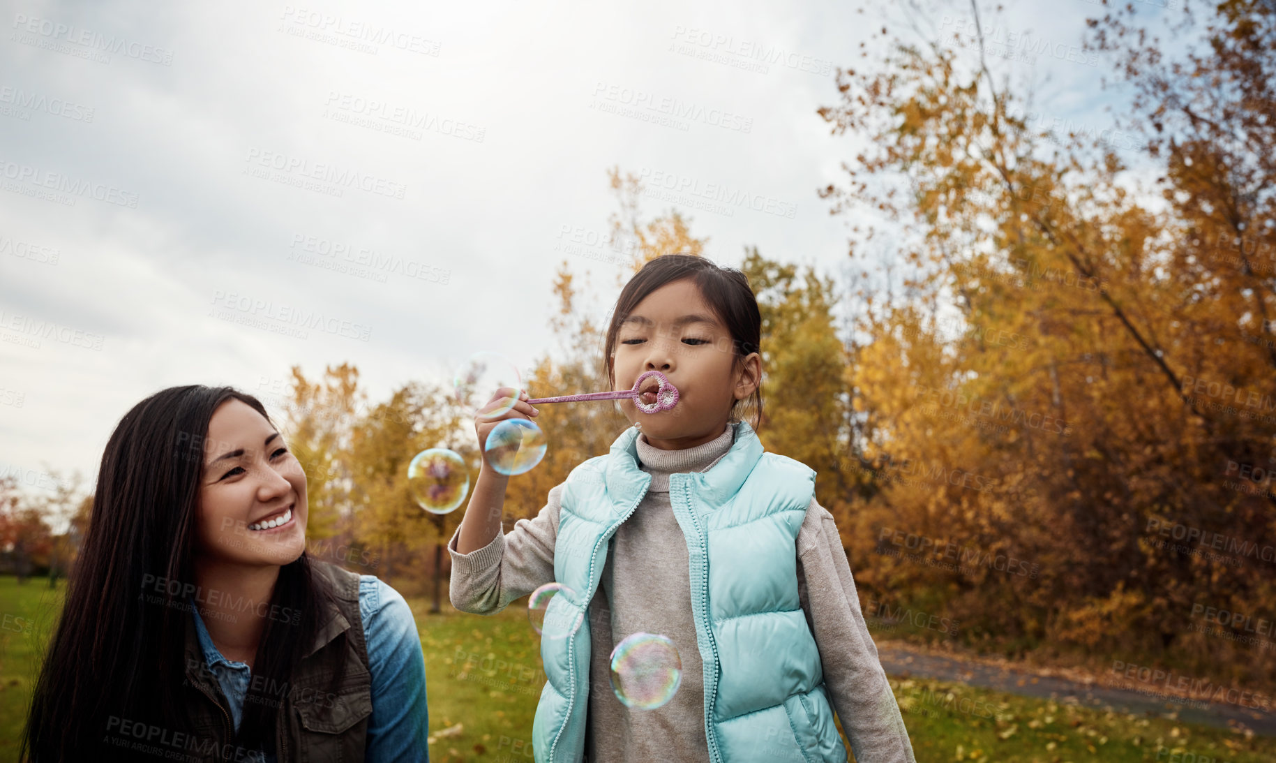 Buy stock photo Shot of a mother and her little daughter playing with bubbles outdoors