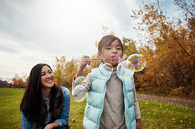 Buy stock photo Shot of a mother and her little daughter playing with bubbles outdoors