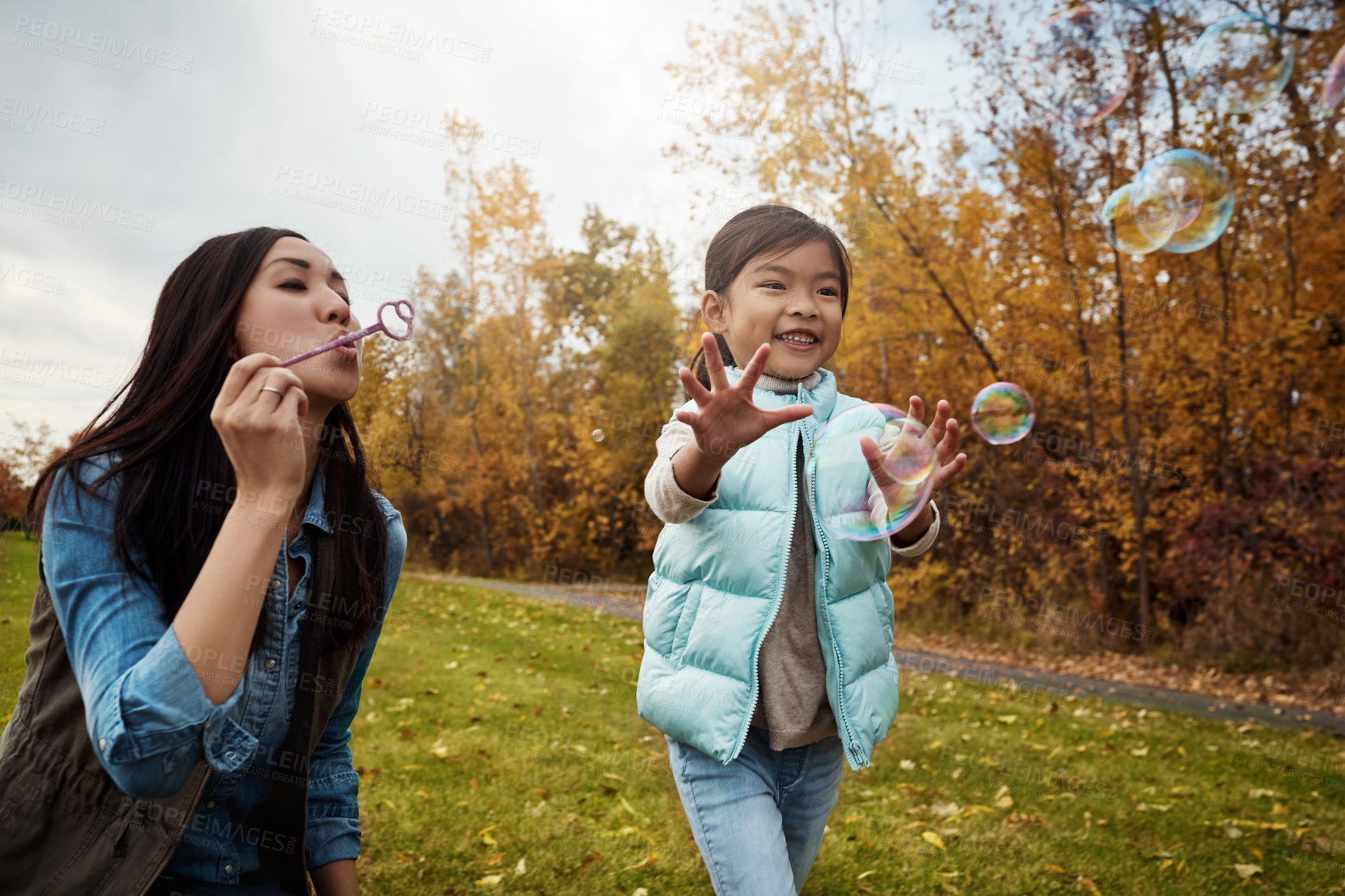 Buy stock photo Shot of a mother and her little daughter playing with bubbles outdoors