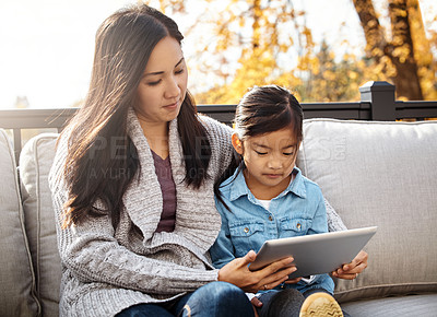 Buy stock photo Shot of an adorable little girl using a digital tablet with her mother on an autumn day outdoors
