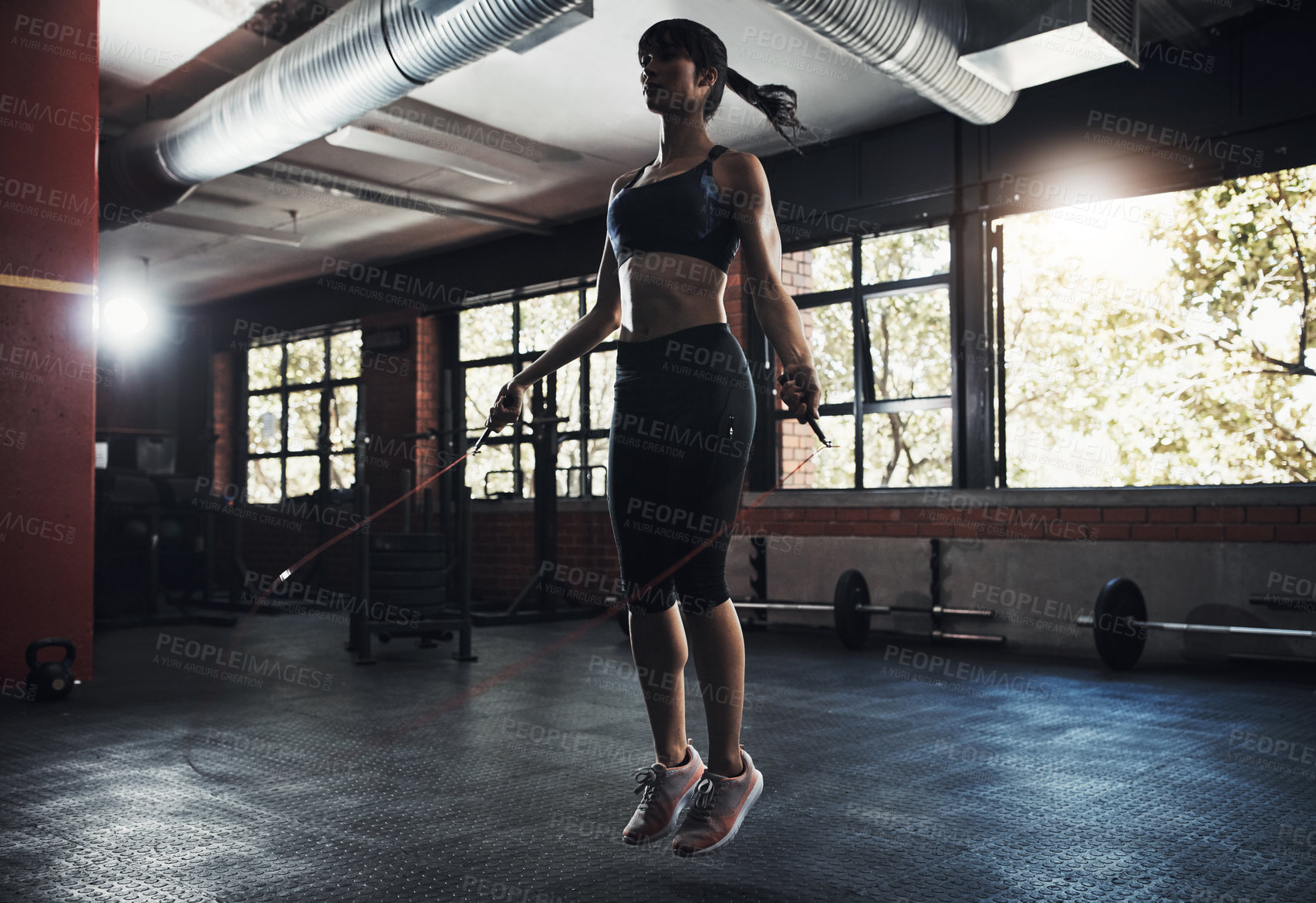 Buy stock photo Shot of a beautiful young woman jumping rope as part of her exercise routine