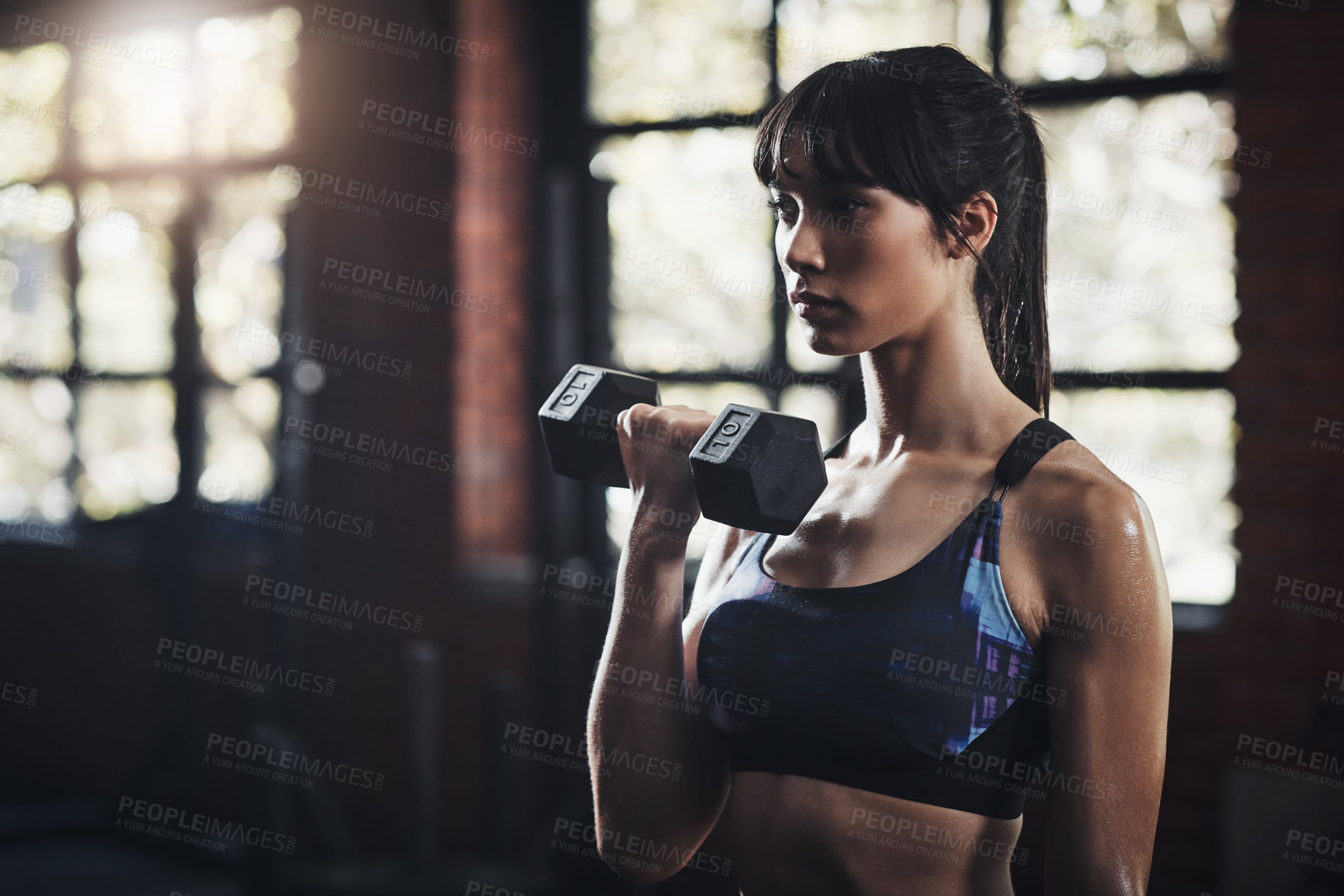 Buy stock photo Cropped shot of a beautiful young woman lifting dumbbells at the gym