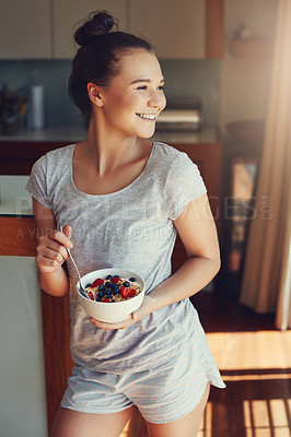 Buy stock photo Shot of an attractive young woman eating her breakfast while standing in the kitchen at home