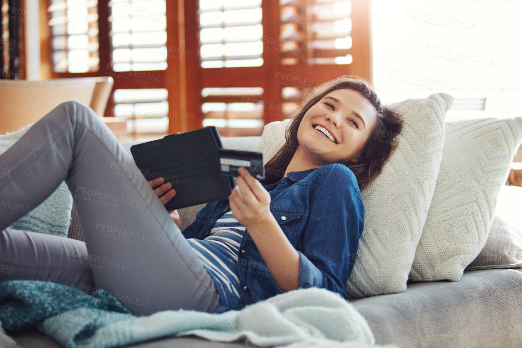 Buy stock photo Shot of an attractive young woman using her tablet to shop online while relaxing on the sofa at home