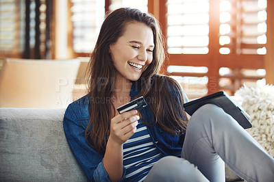 Buy stock photo Shot of an attractive young woman using her tablet to shop online while relaxing on the sofa at home