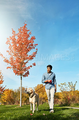 Buy stock photo Shot of a young man taking his dog for a walk through the park