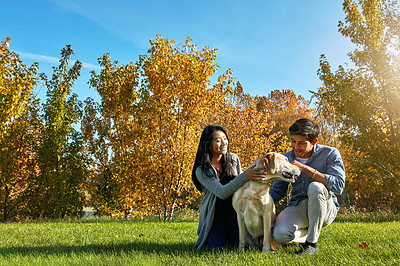 Buy stock photo Shot of a loving young couple taking their dog for a walk through the park