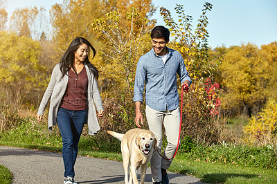 Buy stock photo Shot of a loving young couple taking their dog for a walk through the park