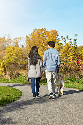 Buy stock photo Shot of a loving young couple taking their dog for a walk through the park