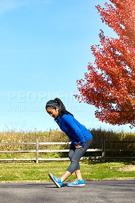 Buy stock photo Shot of a sporty young woman stretching her legs while exercising outdoors