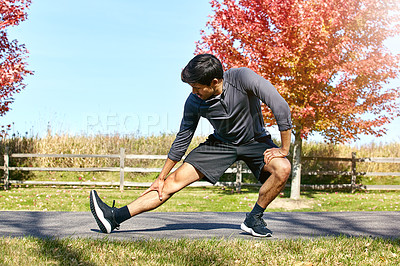 Buy stock photo Shot of a sporty young man stretching his legs while exercising outdoors