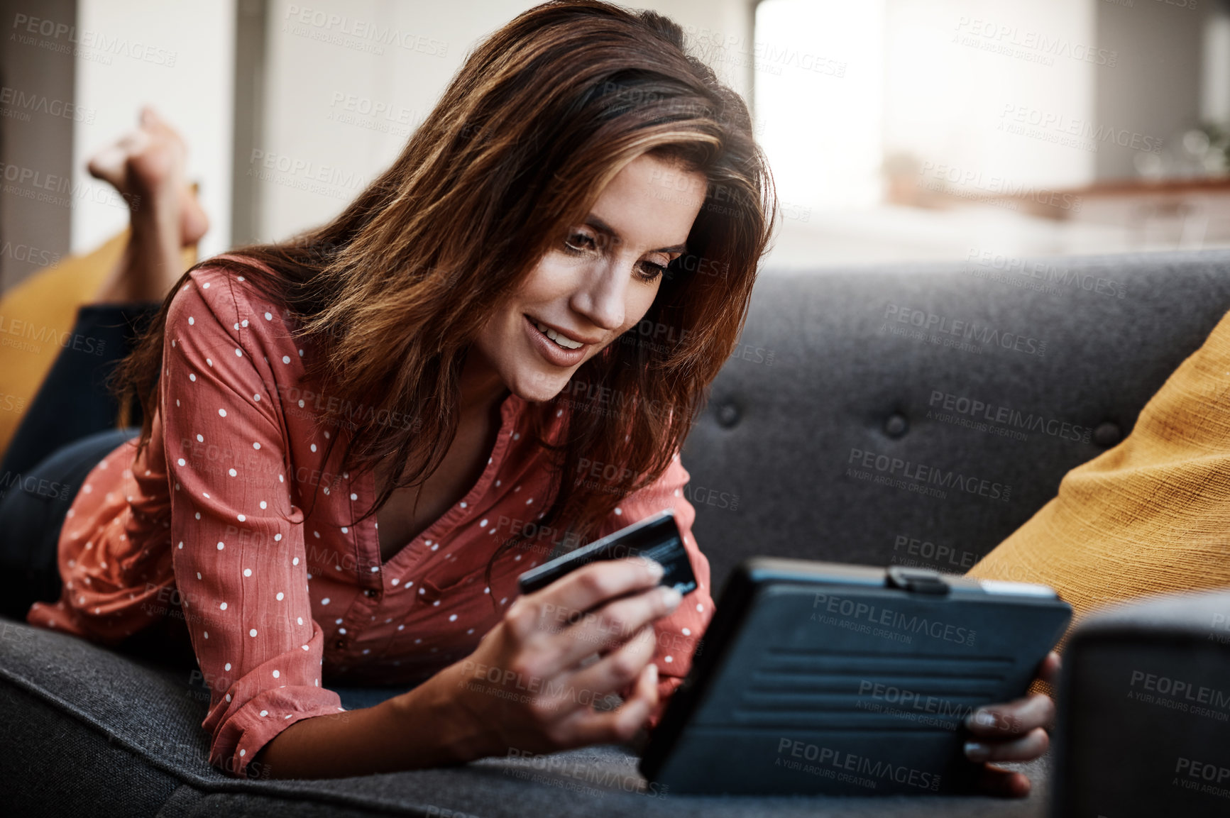 Buy stock photo Shot of an attractive young woman using a digital tablet and credit card on the sofa at home