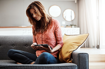 Buy stock photo Shot of an attractive young woman using a digital tablet on the sofa at home