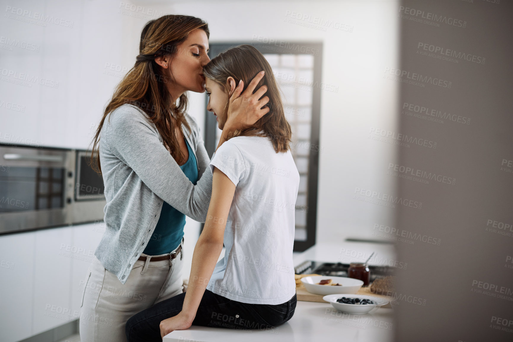 Buy stock photo Cropped shot of an attractive young woman kissing her daughter on the forehead while spending time together at home