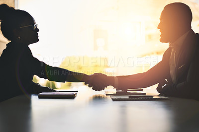 Buy stock photo Silhouetted shot of two businesspeople shaking hands in an office