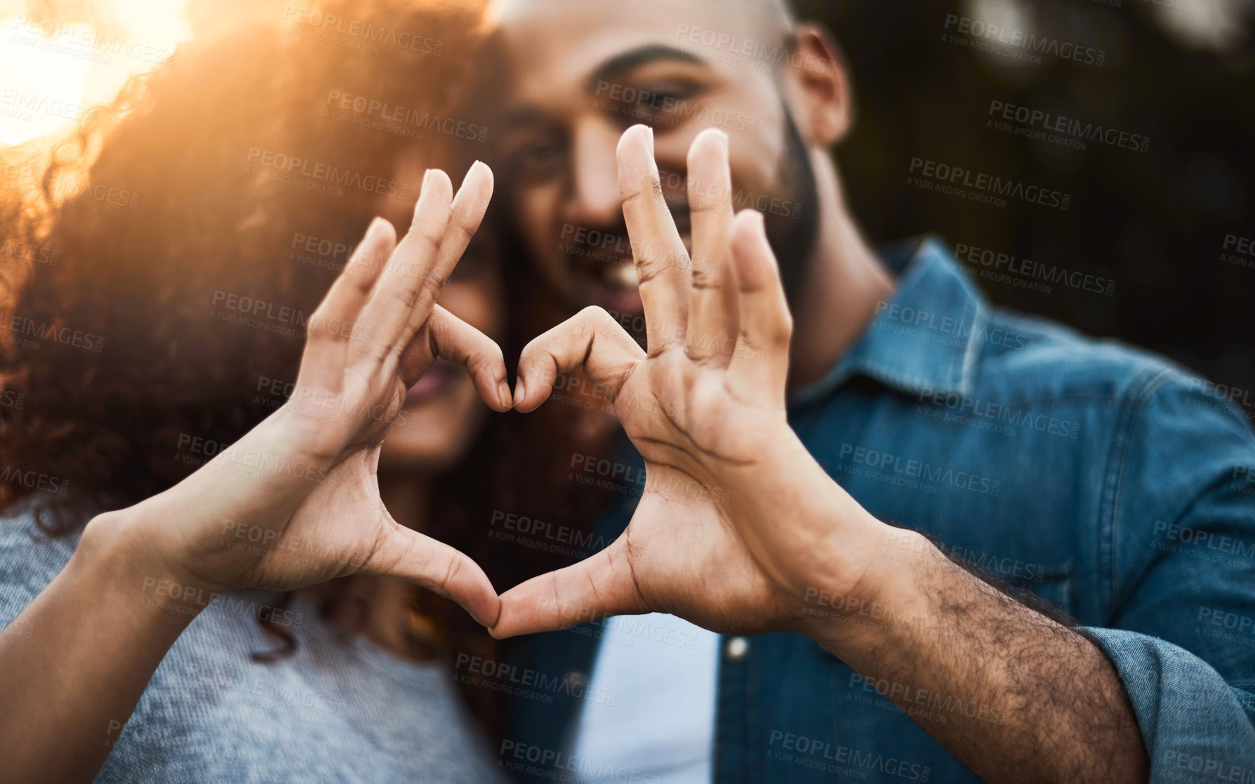 Buy stock photo Shot of a a young couple making a heart shape with their fingers outdoors