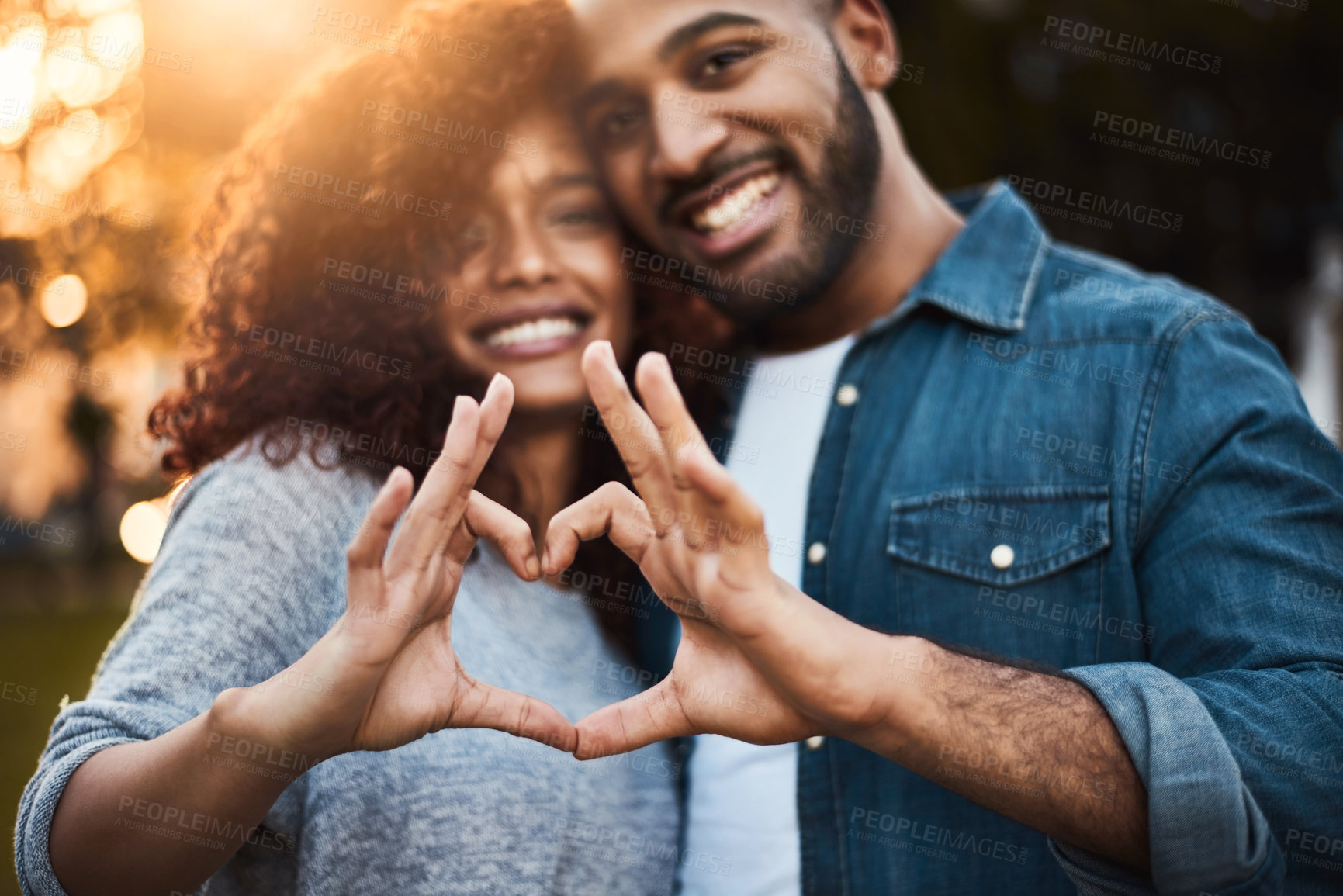 Buy stock photo Portrait of a a young couple making a heart shape with their fingers outdoors