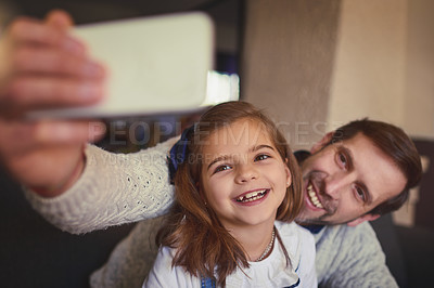 Buy stock photo Cropped shot of a handsome man and his adorable young daughter taking selfies on the sofa at home