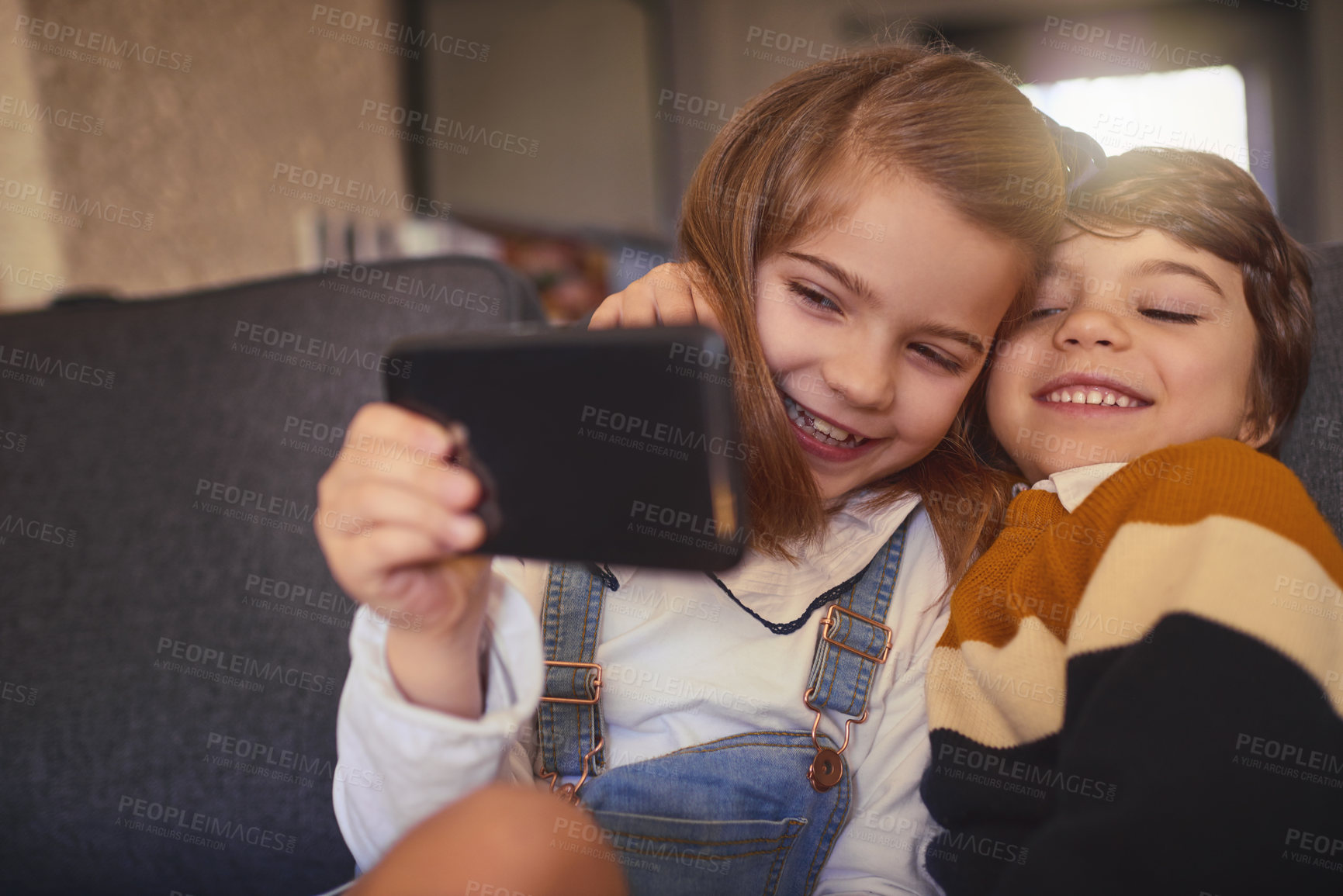 Buy stock photo Cropped shot of an adorable little girl and her younger brother taking selfies while sitting on the sofa at home