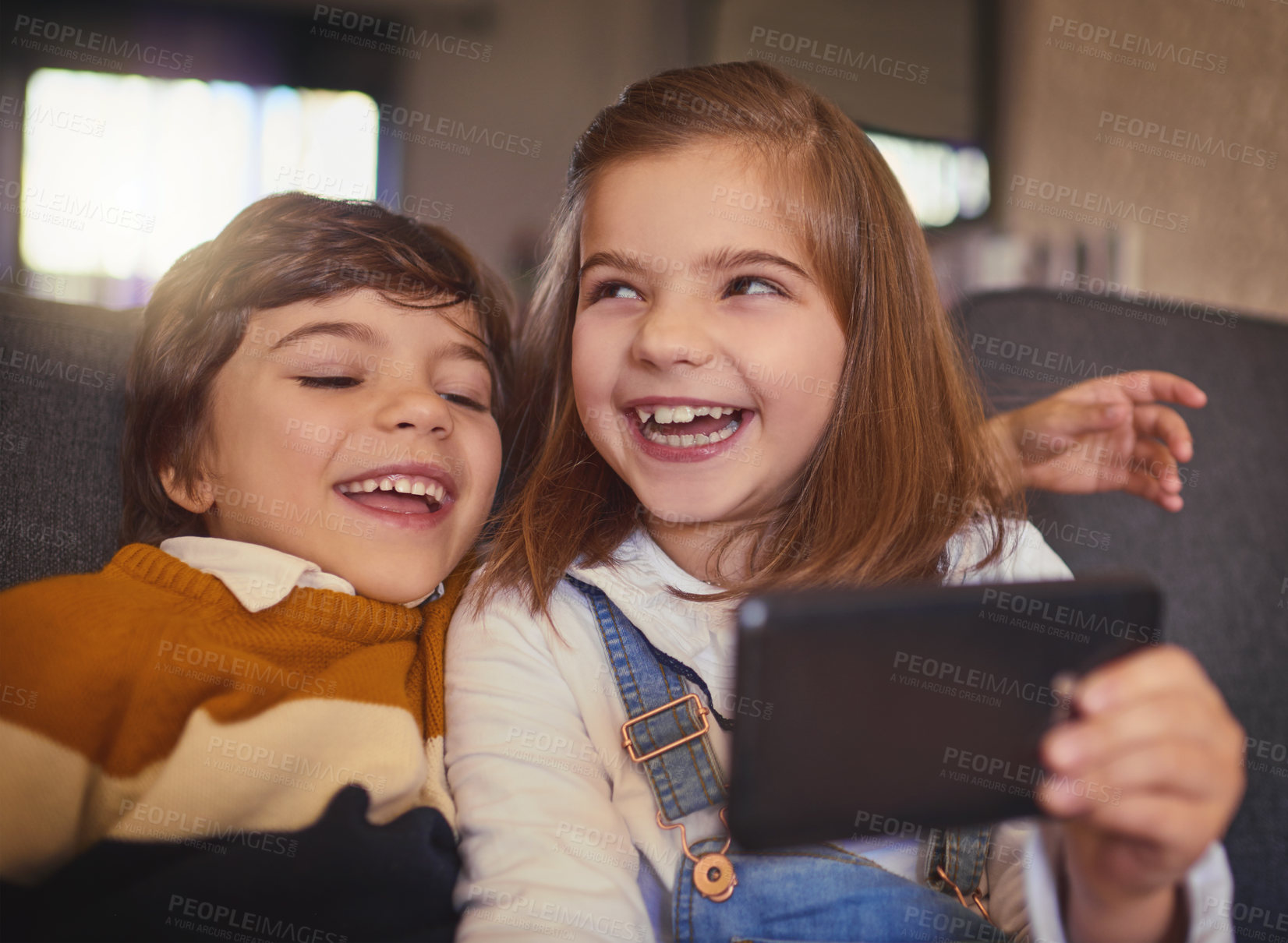 Buy stock photo Cropped shot of an adorable little girl and her younger brother taking selfies while sitting on the sofa at home