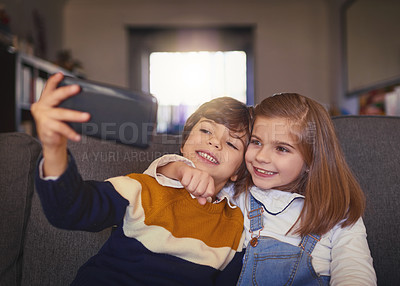 Buy stock photo Cropped shot of an adorable little boy and his older sister taking selfies while sitting on the sofa at home