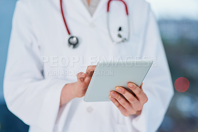 Buy stock photo Cropped shot of an unrecognizable female doctor using a tablet while standing in the hospital