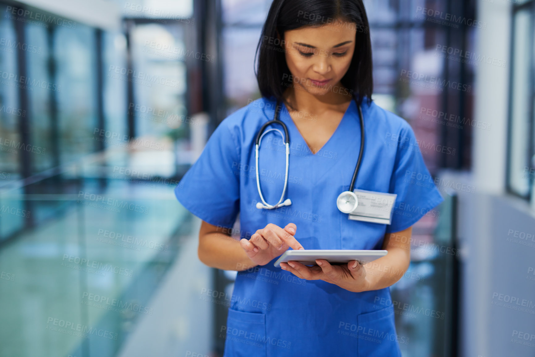 Buy stock photo Cropped shot of an attractive young female nurse using a tablet while standing in the hospital