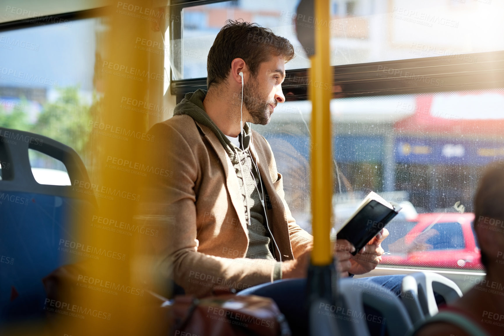 Buy stock photo Cropped shot of a handsome young man reading a book during his morning bus commute