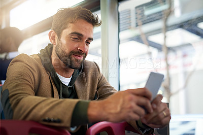 Buy stock photo Cropped shot of a handsome young man sending a text message during his morning bus commute