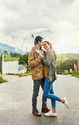 Buy stock photo Shot of a loving couple standing outside with an umbrella