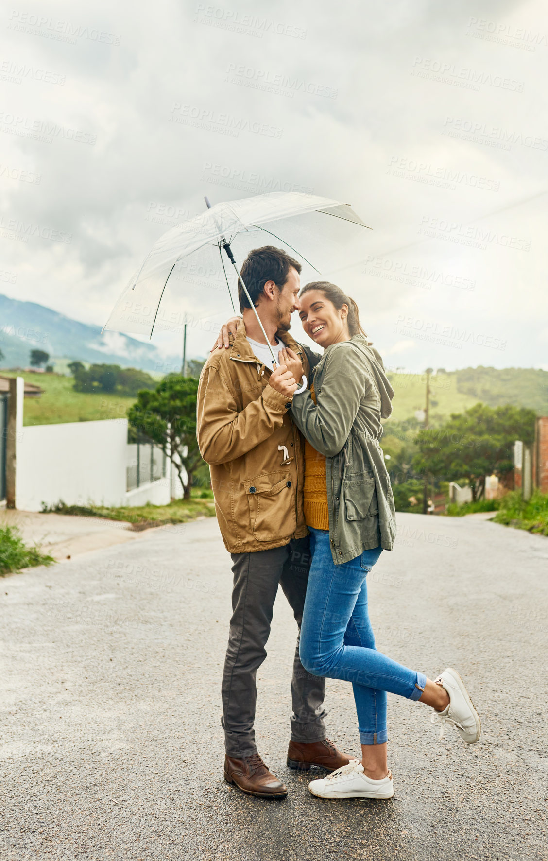 Buy stock photo Shot of a loving couple standing outside with an umbrella