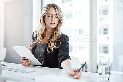 Buy stock photo Shot of a young businesswoman using a digital tablet and writing notes at her desk in a modern office