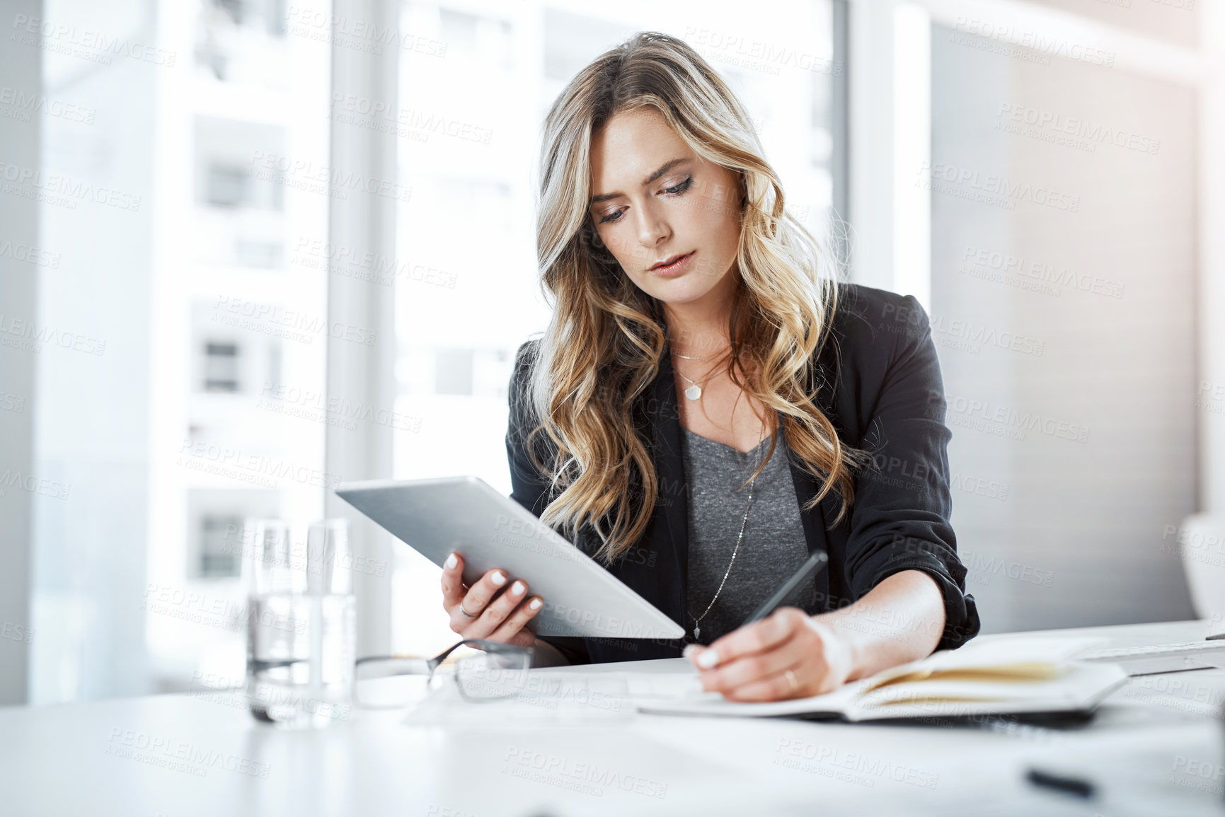 Buy stock photo Shot of a young businesswoman using a digital tablet and writing notes at her desk in a modern office