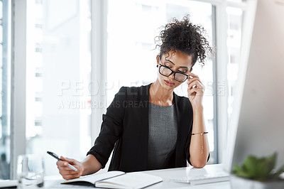Buy stock photo Shot of a young businesswoman using a computer and writing notes at her desk in a modern office