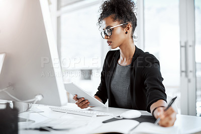 Buy stock photo Shot of a young businesswoman using a digital tablet, computer and writing notes at her desk in a modern office