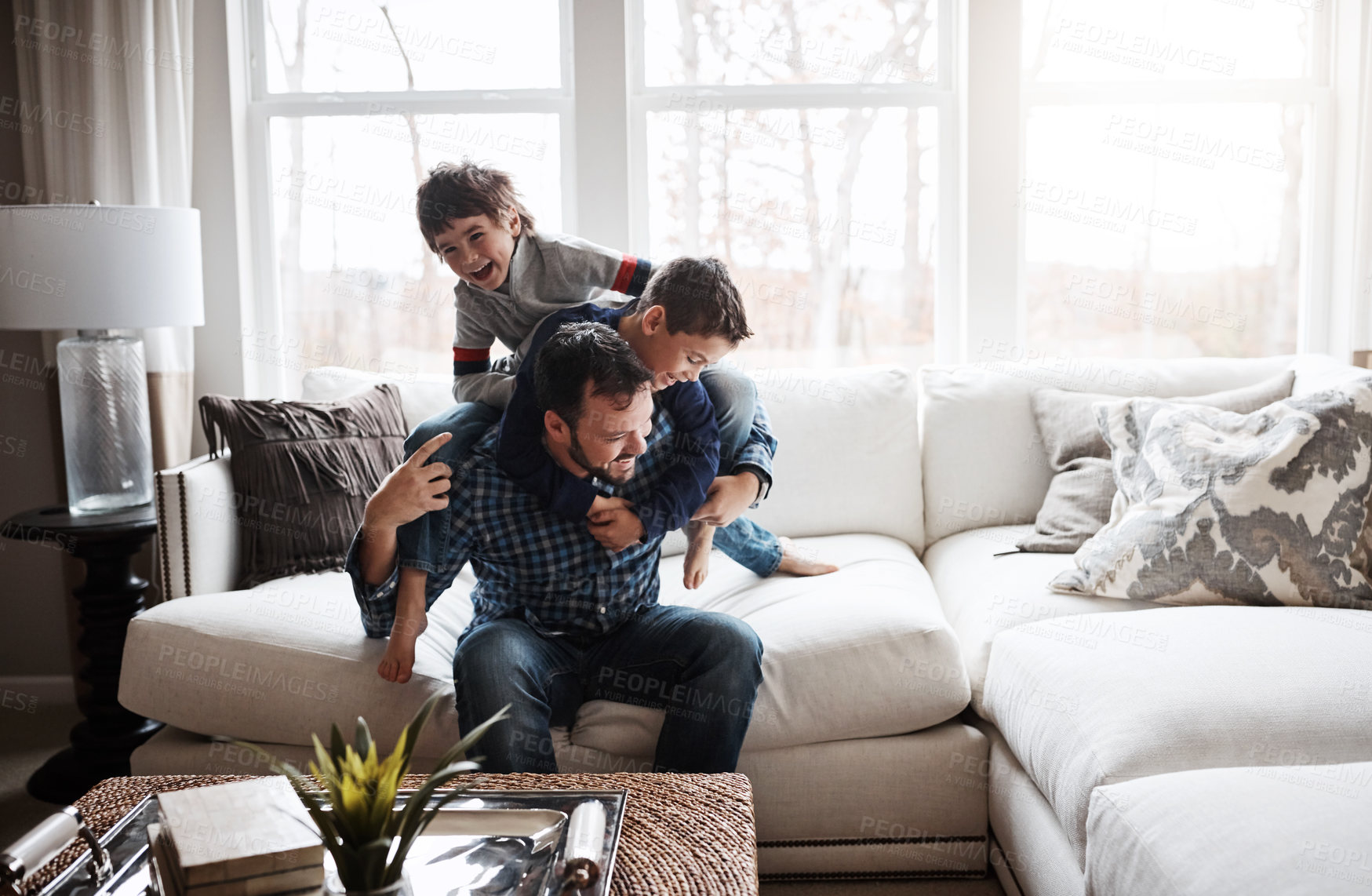Buy stock photo Playful, bonding and father with children on the sofa for playing, quality time and crazy fun. Love, happy and boy kids piling onto their dad with energy on the couch of their family home together