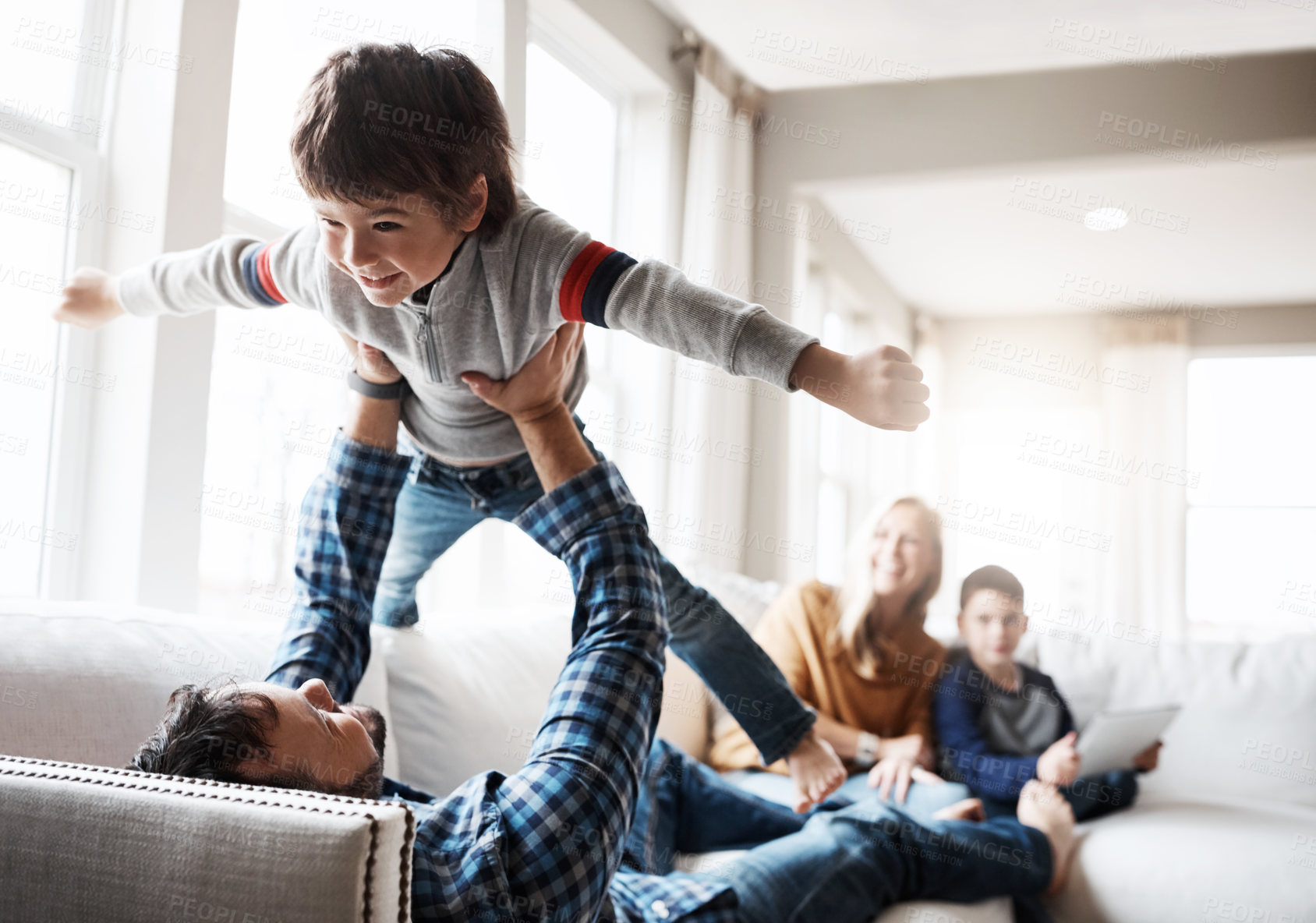 Buy stock photo Wellness, relax and father lifting child on sofa for bonding, fun and play in happy home. Dad playing flying plane in air game with son on living room couch for care, love and bond together