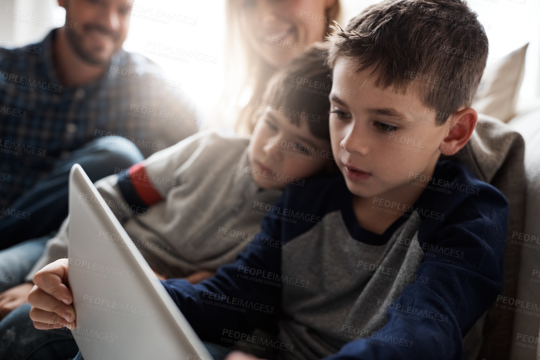 Buy stock photo Shot of two adorable brothers using a digital tablet together with their parents on the sofa at home