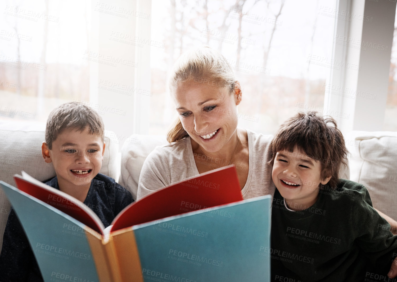 Buy stock photo Shot of two adorable brothers reading a book together with their mother while relaxing on the sofa at home