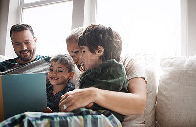 Buy stock photo Shot of two adorable brothers reading a book together with their parents while relaxing on the sofa at home