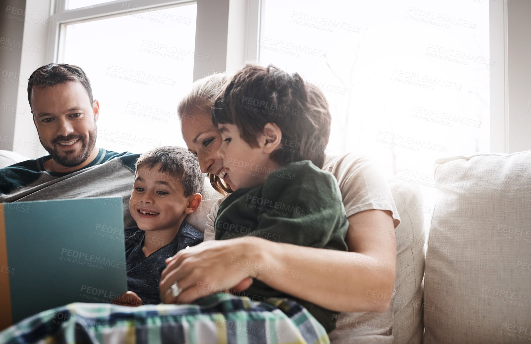 Buy stock photo Shot of two adorable brothers reading a book together with their parents while relaxing on the sofa at home