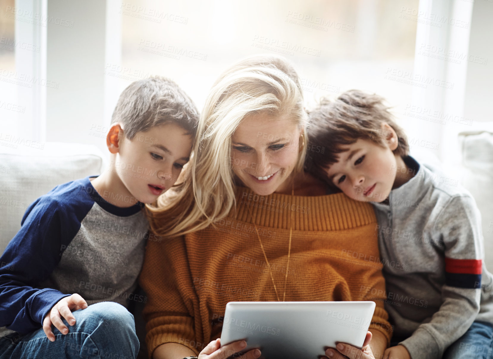 Buy stock photo Shot of two adorable brothers using a digital tablet together with their mother while relaxing on the sofa at home
