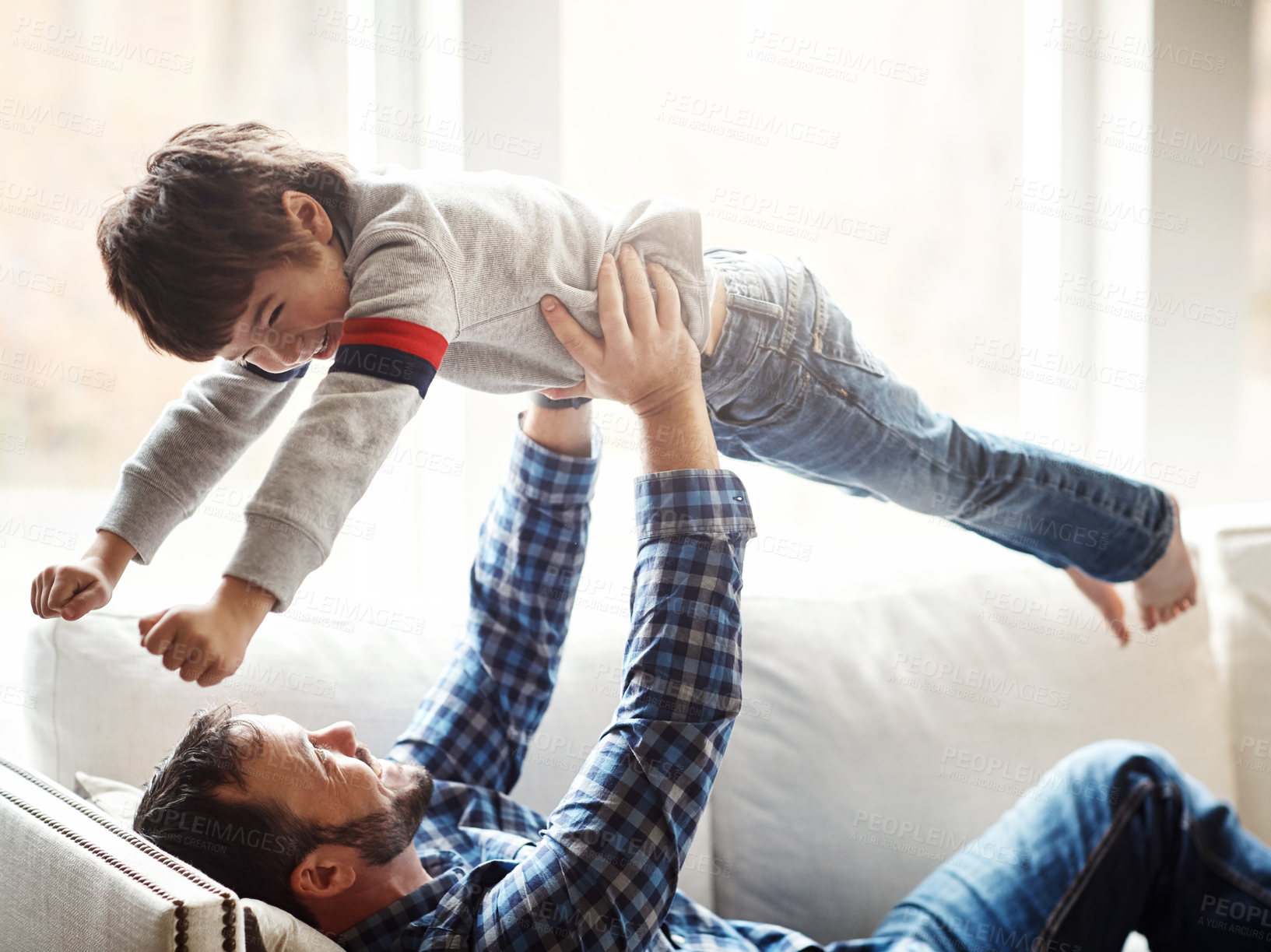 Buy stock photo Shot of an adorable little boy having fun with his father on the sofa at home