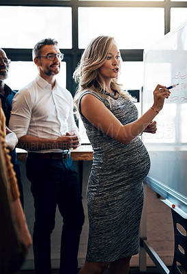 Buy stock photo Pregnant businesswoman doing a presentation in a meeting planning the company growth strategy in an office. Serious female entrepreneur briefing her team on the startup project mission and vision