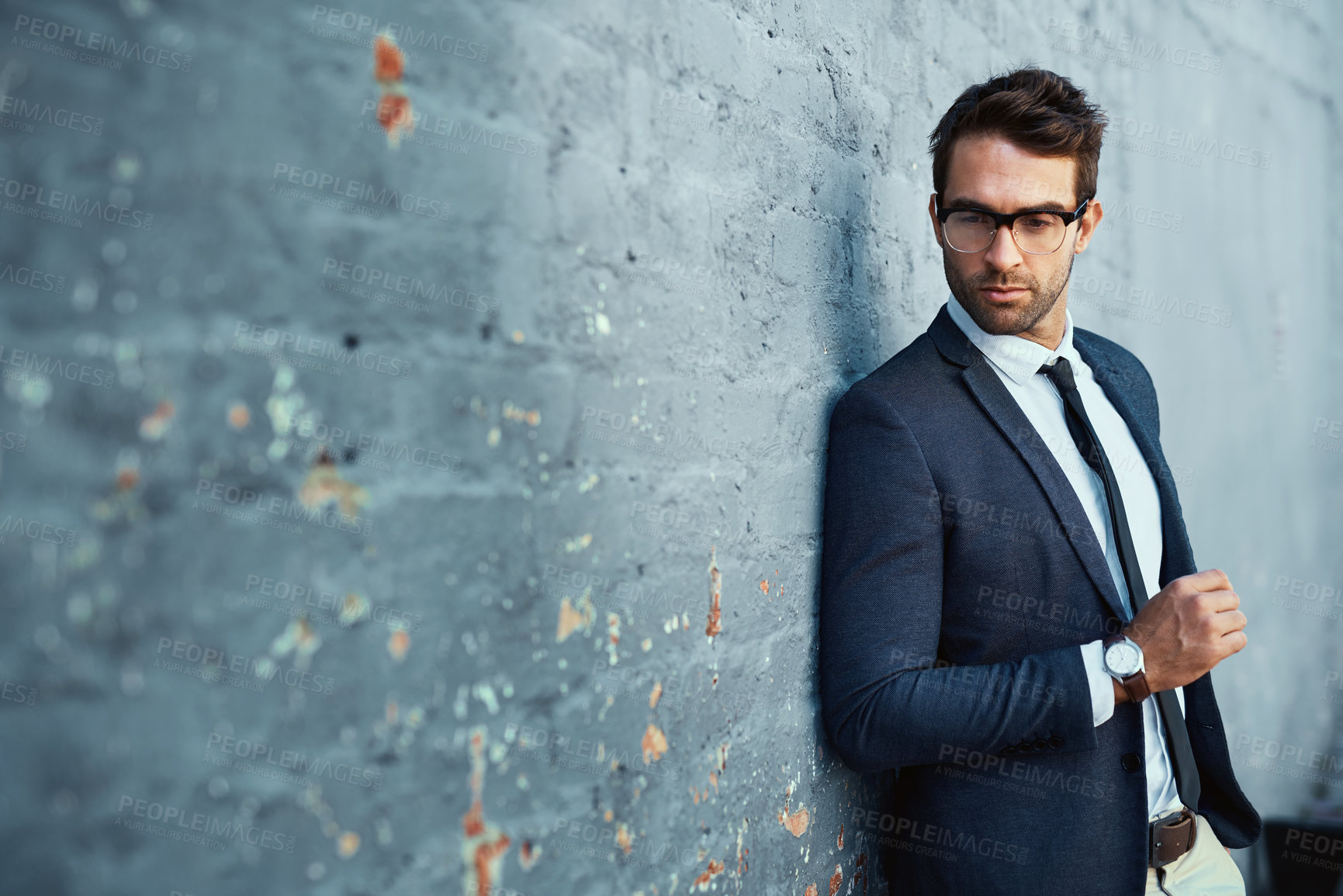 Buy stock photo Cropped shot of a handsome young businessman standing against a grey facebrick wall