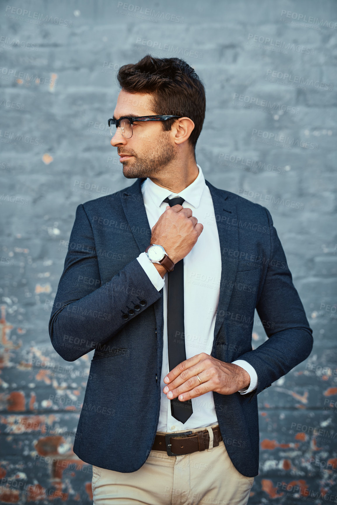 Buy stock photo Cropped shot of a handsome young businessman adjusting his tie while standing against a grey facebrick wall