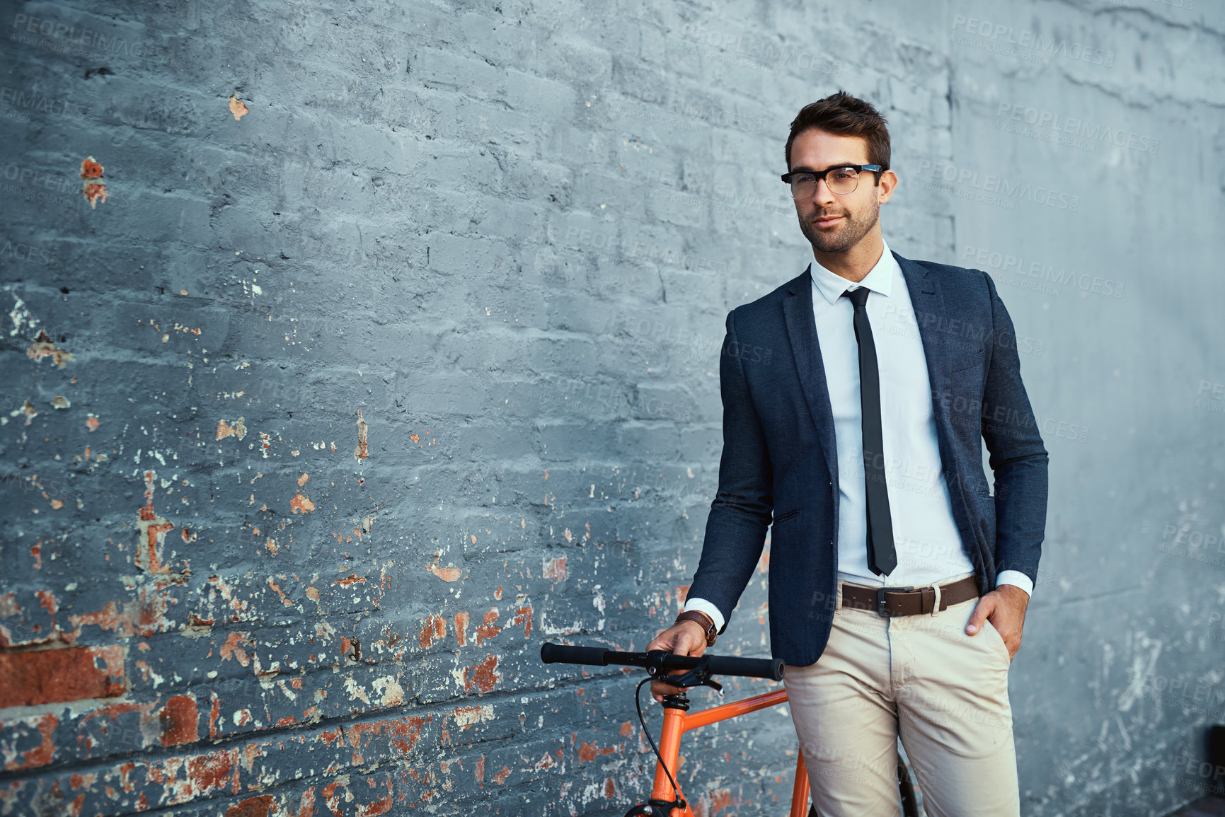 Buy stock photo Cropped shot of a handsome young businessman standing with his bicycle against a grey facebrick wall