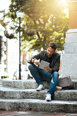 Buy stock photo Full length shot of a handsome young man using his tablet while traveling through the city