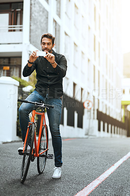 Buy stock photo Full length shot of a handsome young man taking photographs while traveling through the city by bike