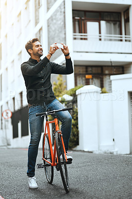 Buy stock photo Full length shot of a handsome young man taking photographs while traveling through the city by bike